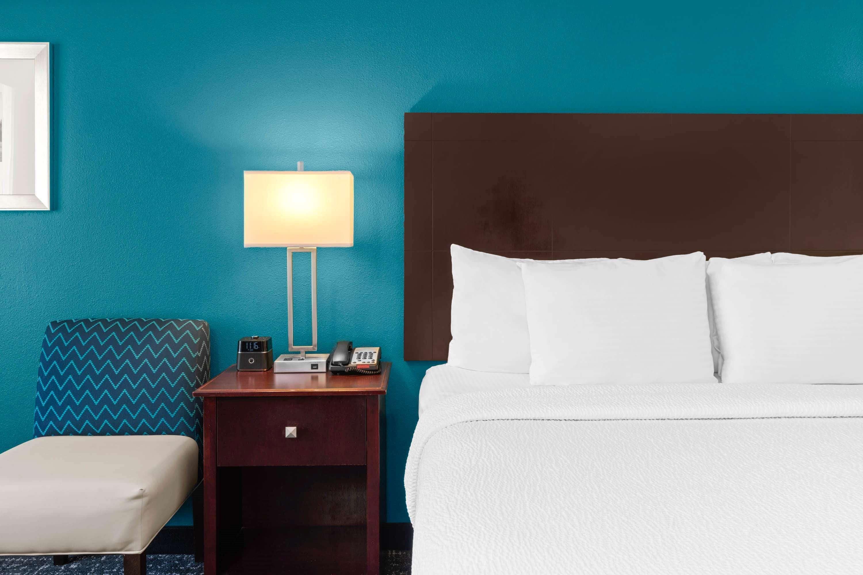 Una habitación de hotel con una cama, una mesita de noche con lámpara, un teléfono y una silla.