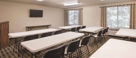A conference room with multiple tables and chairs, a flat-screen TV on the wall, and large windows with curtains.