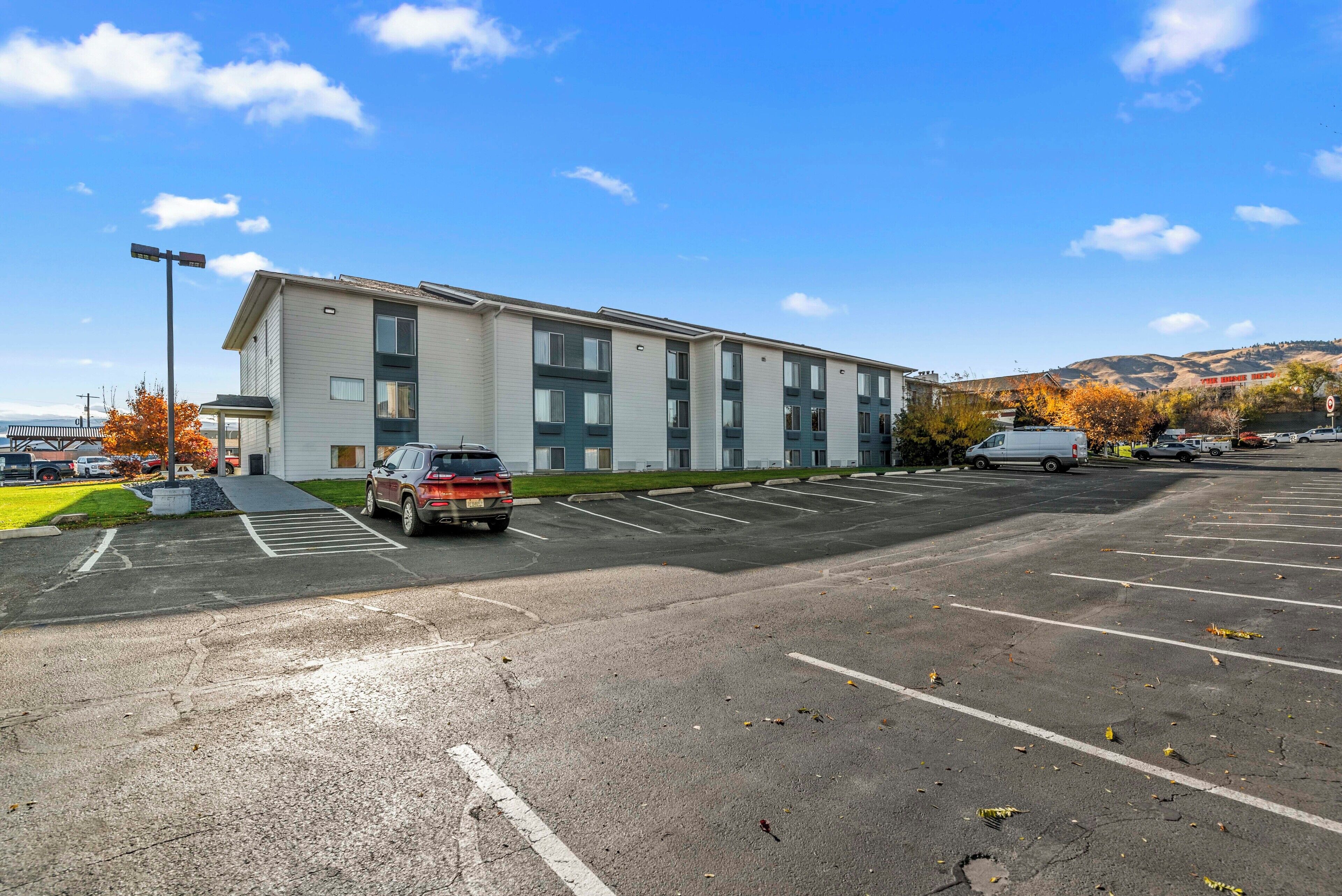 A parking lot with a row of single-story buildings, a clear sky, and autumn foliage.