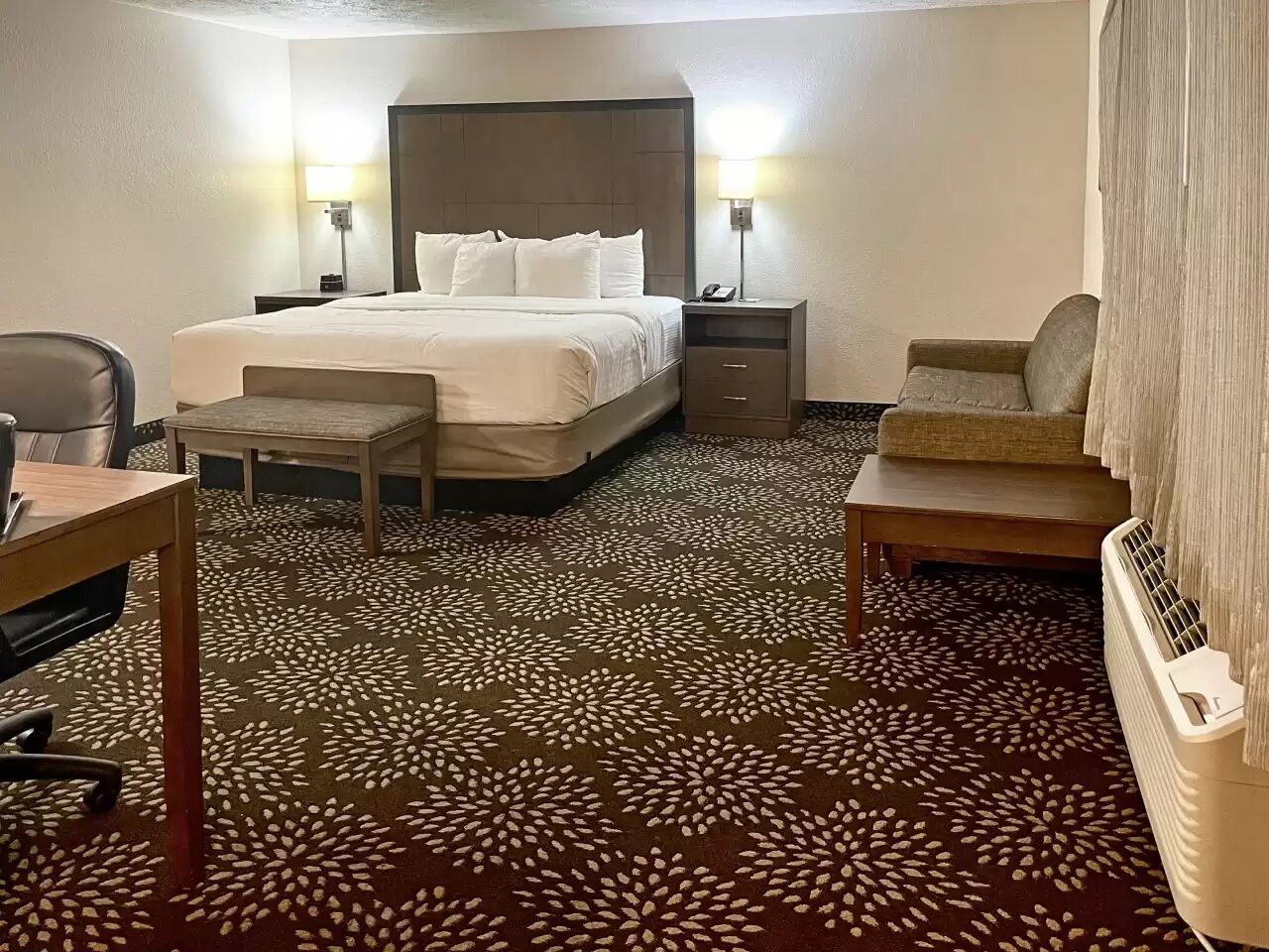 Ein Hotelzimmer mit Bett, Nachttischen, Schreibtisch, Stuhl und Heizkörper.