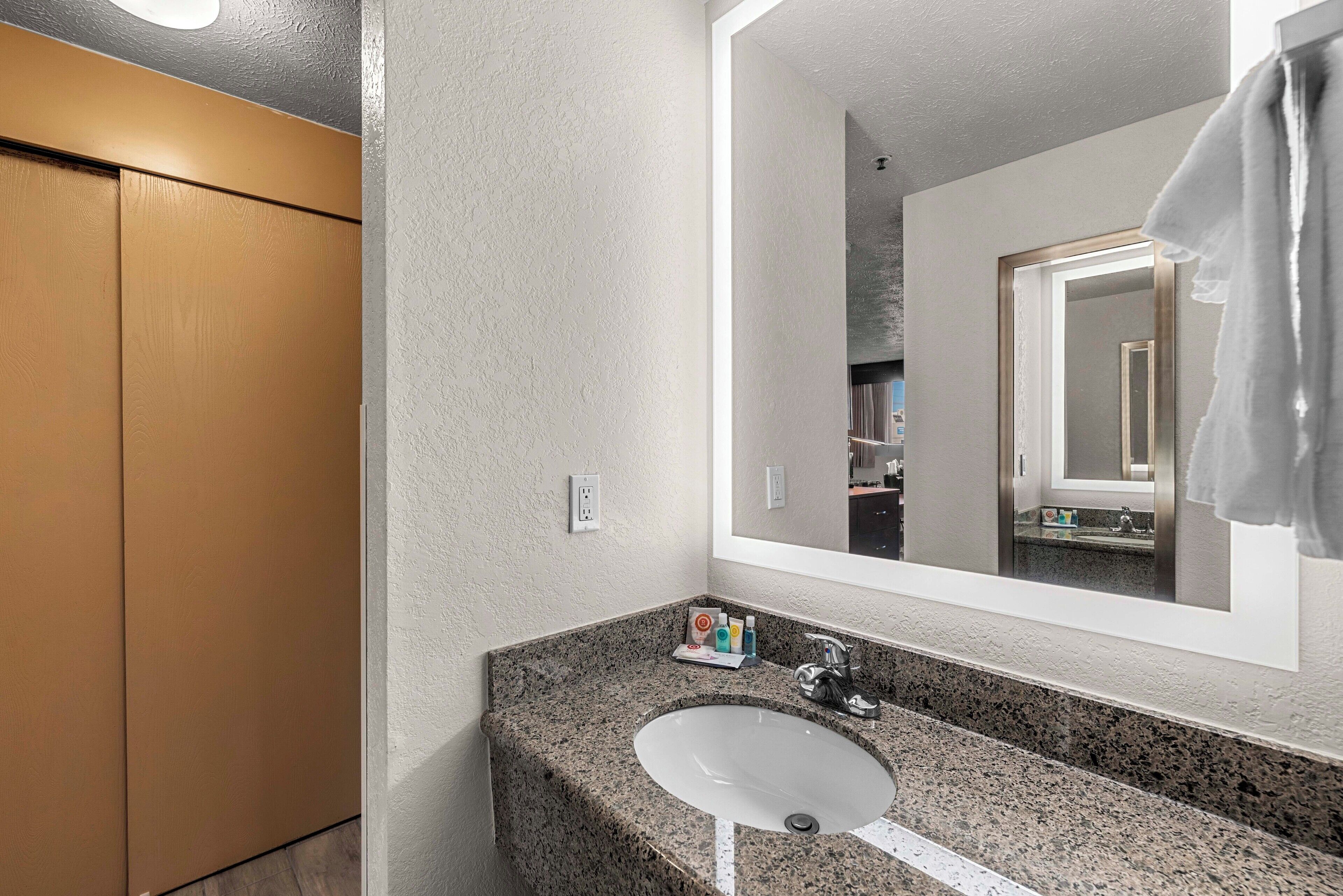 A bathroom with a granite countertop sink, a large mirror, and a towel hanging on the wall.