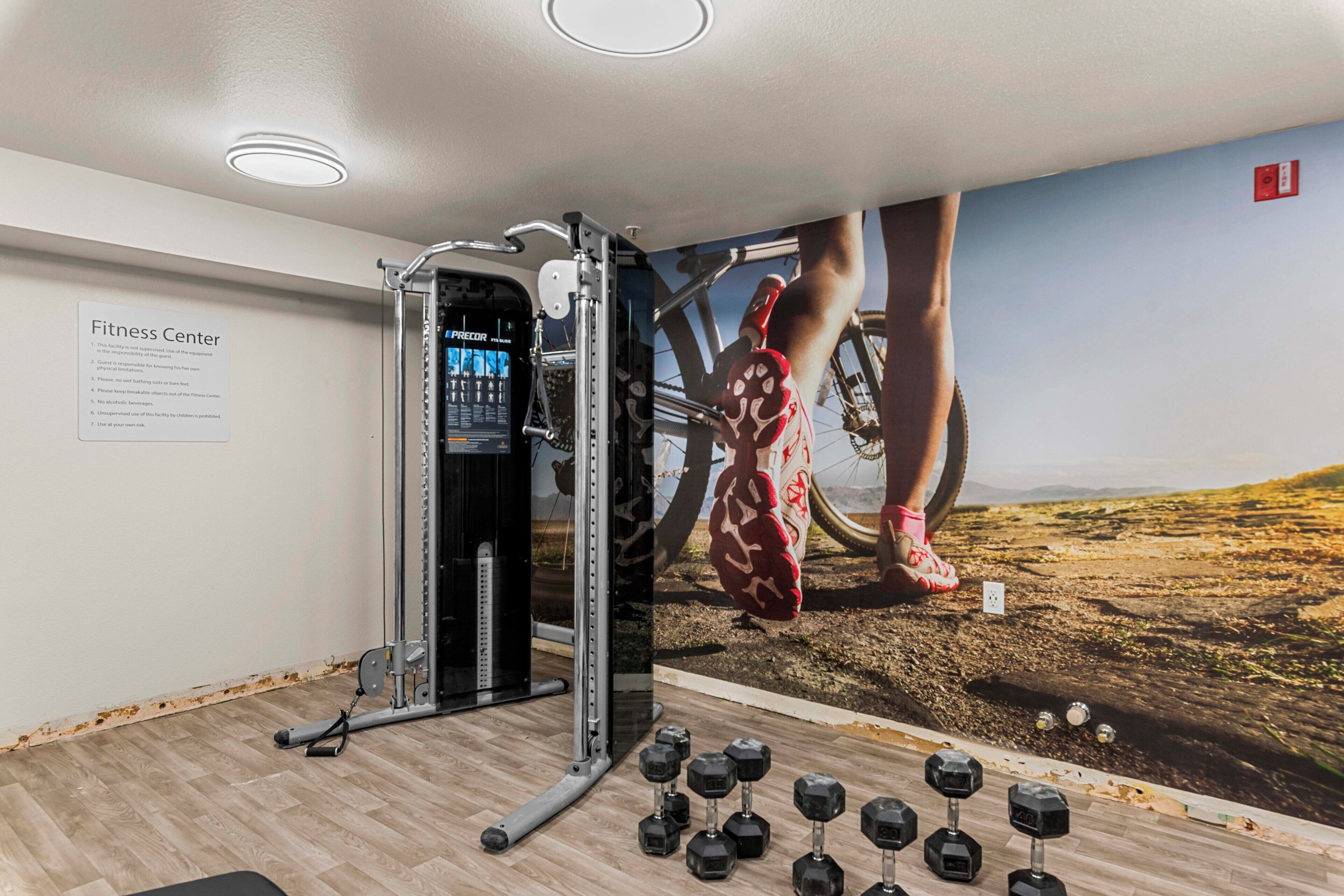 A fitness center with a wall-mounted exercise machine, dumbbells, and a poster of a person exercising.