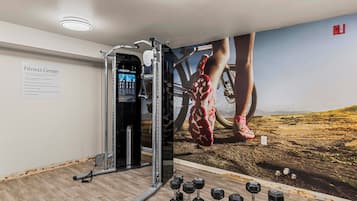 A fitness center with a wall-mounted exercise machine, dumbbells, and a poster of a person exercising.