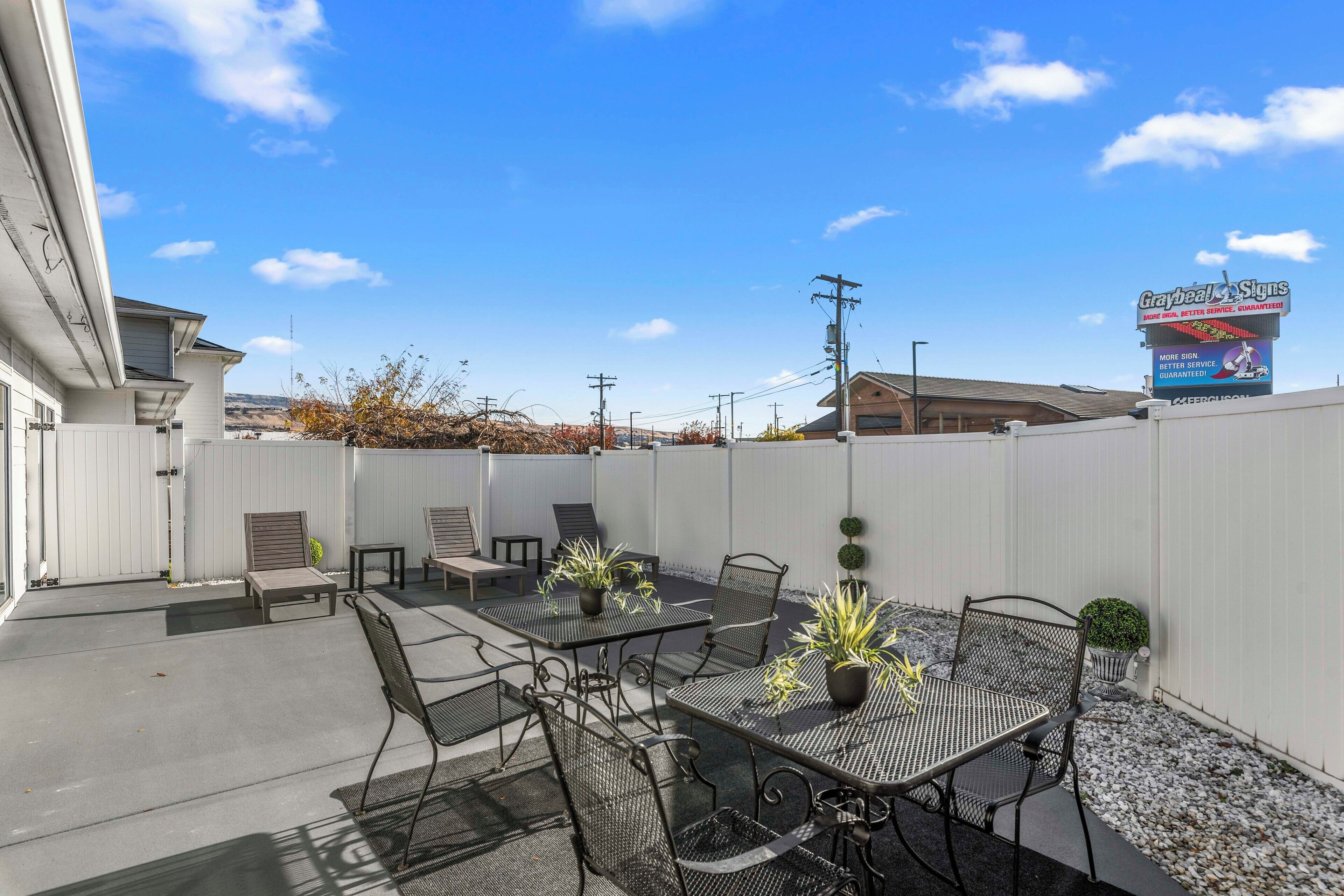 Un patio con mobiliario exterior, incluyendo mesas y sillas, rodeado por una valla blanca.