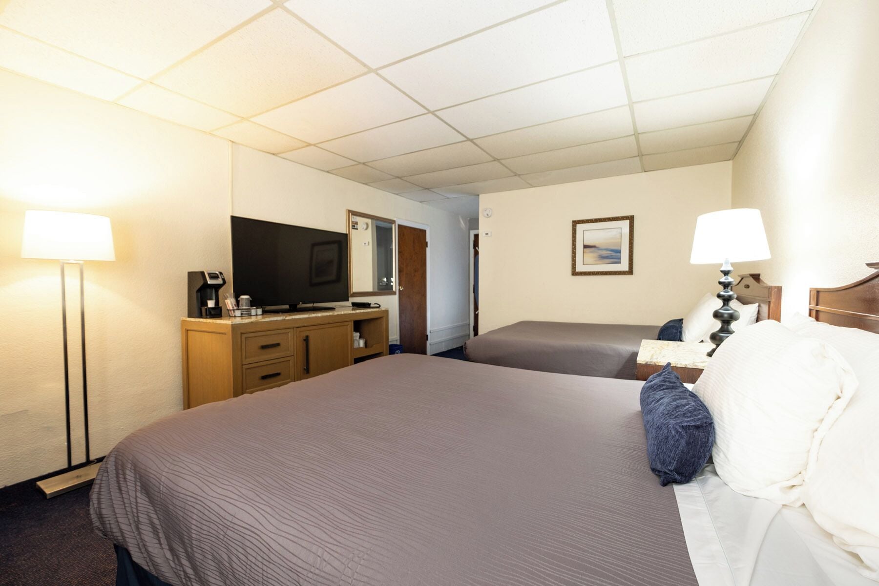 Habitación de hotel con dos camas, un televisor, un escritorio con computadora y una lámpara.
