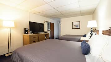 Habitación de hotel con dos camas, un televisor, un escritorio con computadora y una lámpara.