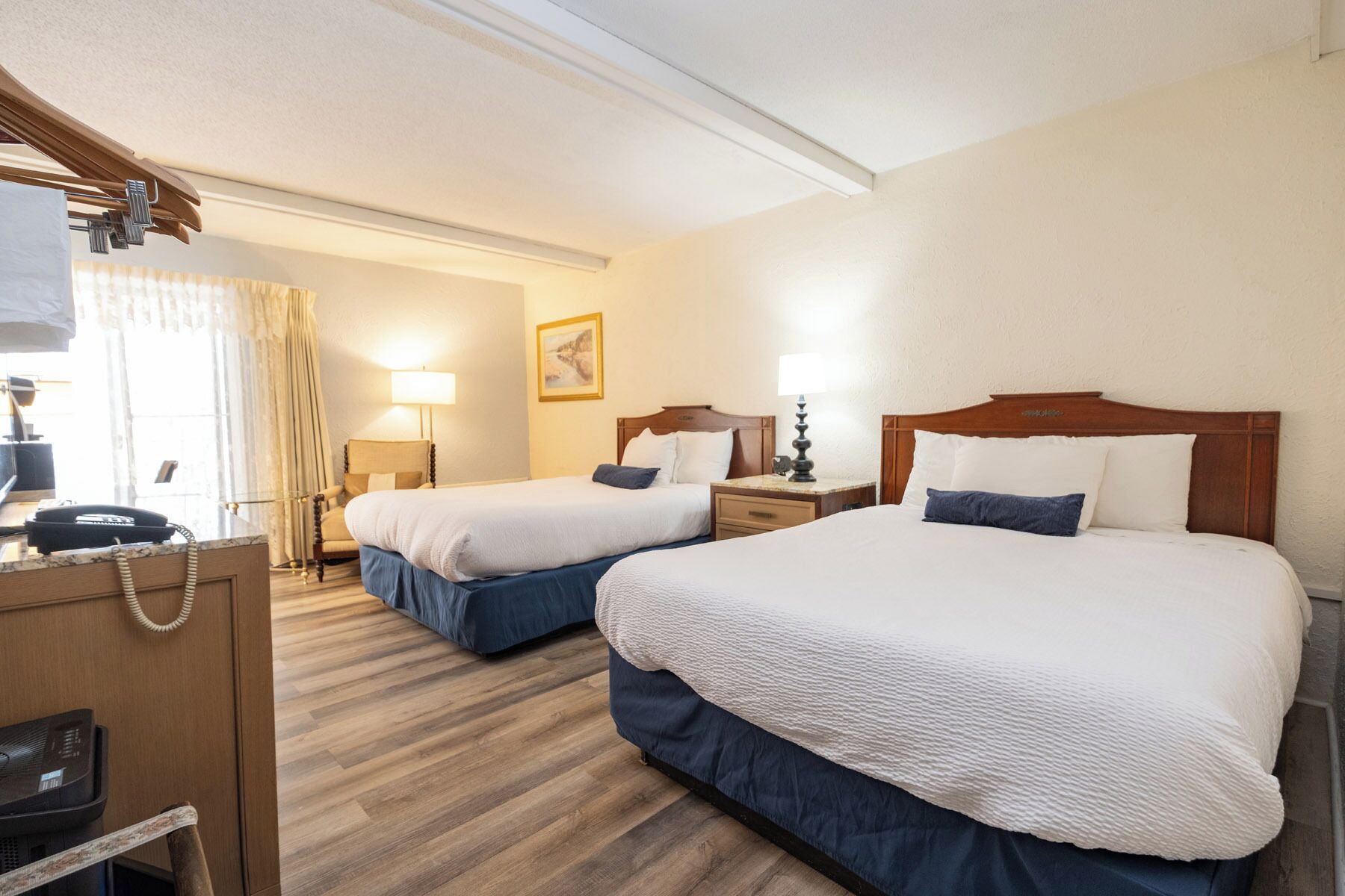 Une chambre d’hôtel avec deux lits, un bureau, une chaise, une lampe et un tableau au mur.