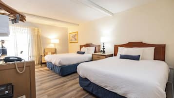Une chambre d’hôtel avec deux lits, un bureau, une chaise, une lampe et un tableau au mur.