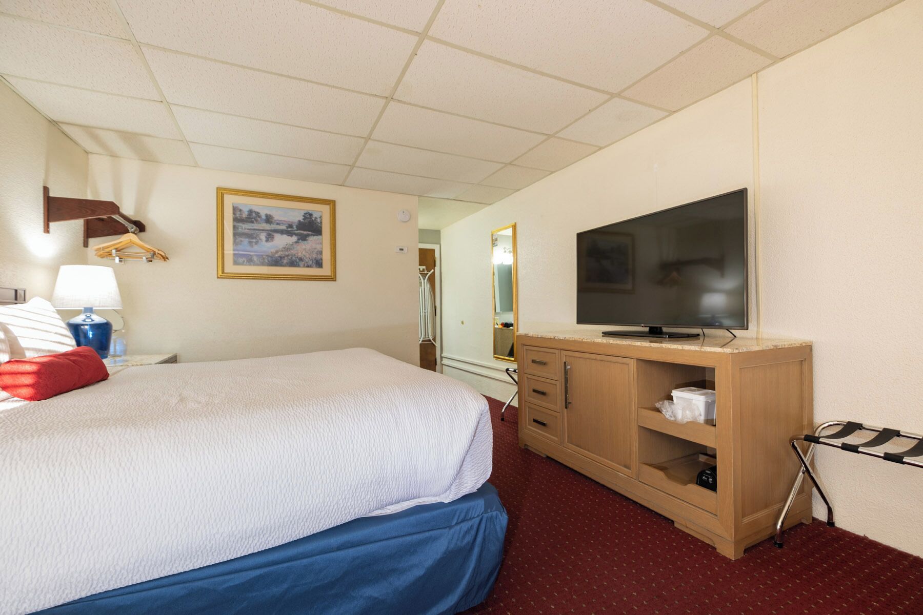 A hotel room with a bed, a TV, a wooden dresser, and a mirror.