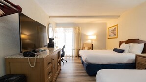 A hotel room with a desk, two beds, a mirror, a lamp, and a window with curtains. - Fireside Inn & Suites Bangor (Bangor)