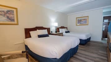 A hotel room with two beds, a wooden floor, and a painting on the wall.