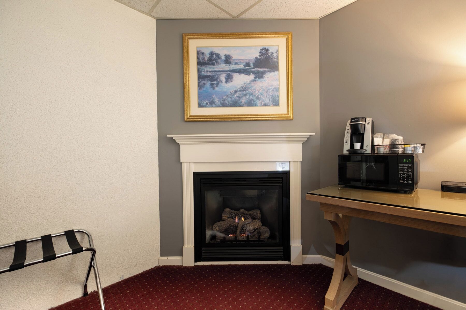 Una habitación con chimenea, un cuadro enmarcado encima, un microondas sobre una mesa y una alfombra roja.