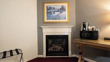 Una habitación con chimenea, un cuadro enmarcado encima, un microondas sobre una mesa y una alfombra roja.