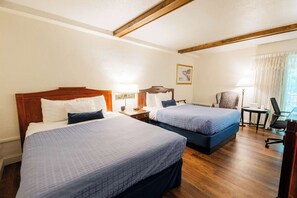 A hotel room with two beds, wooden headboards, and a small desk with a chair.