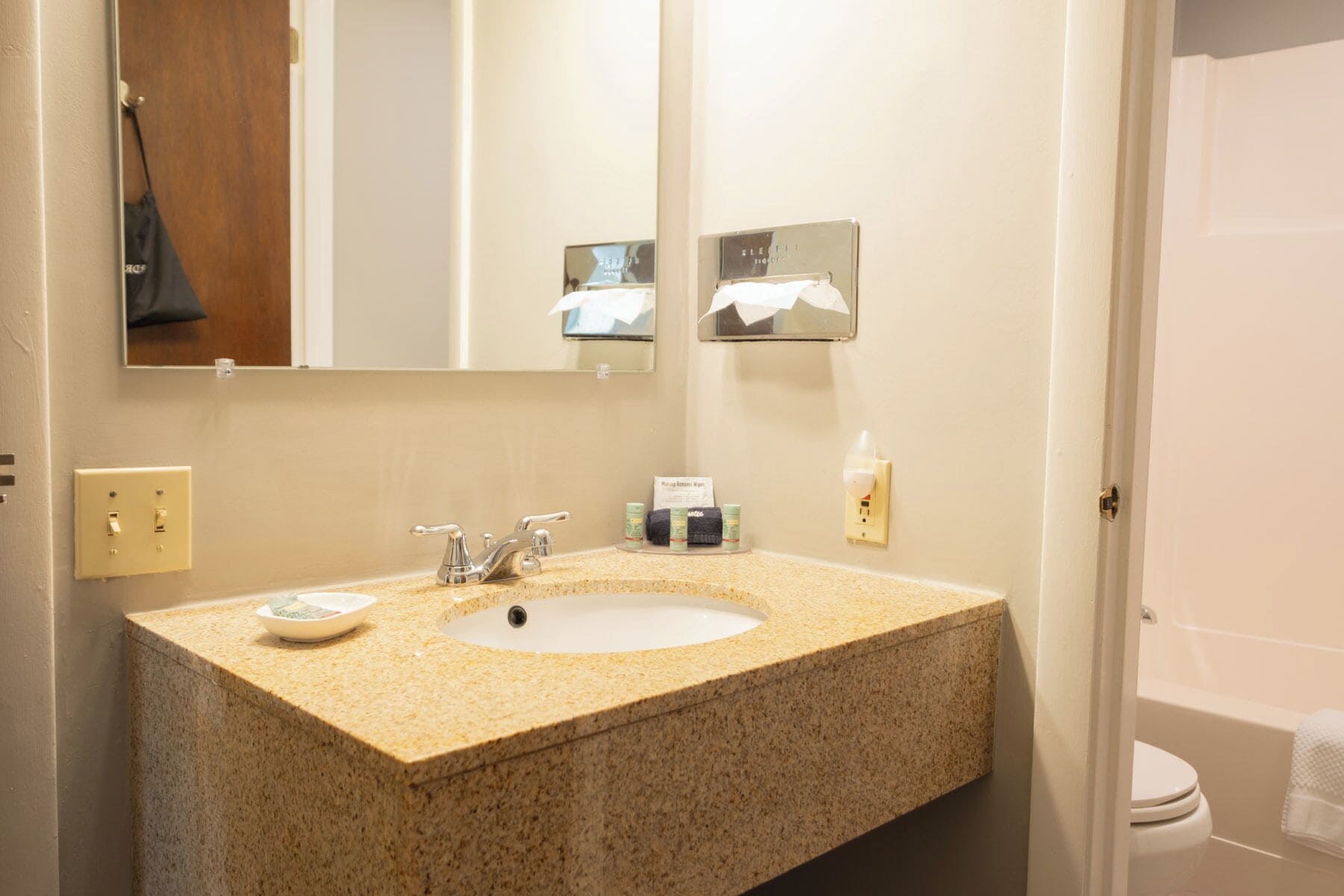 A bathroom with a granite countertop sink, a mirror, and a toilet.