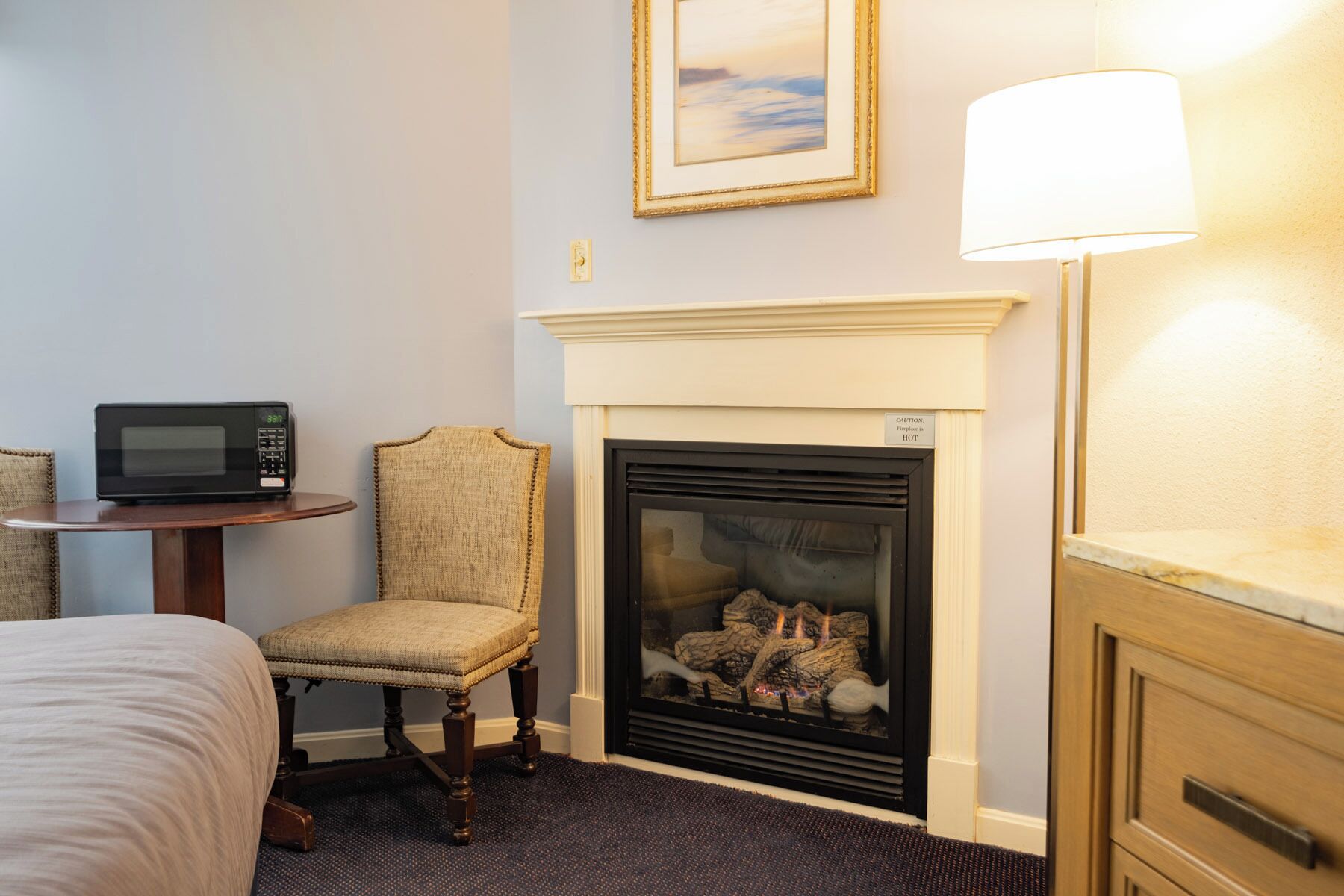 Une chambre d’hôtel équipée d’une cheminée, d’un four à micro-ondes, d’une chaise, d’un lit et d’une lampe.