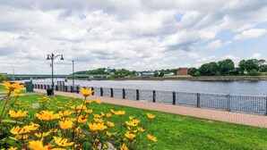 A riverside walkway with a brick path, metal railing, and yellow flowers in the foreground. - Fireside Inn & Suites Bangor (Bangor)