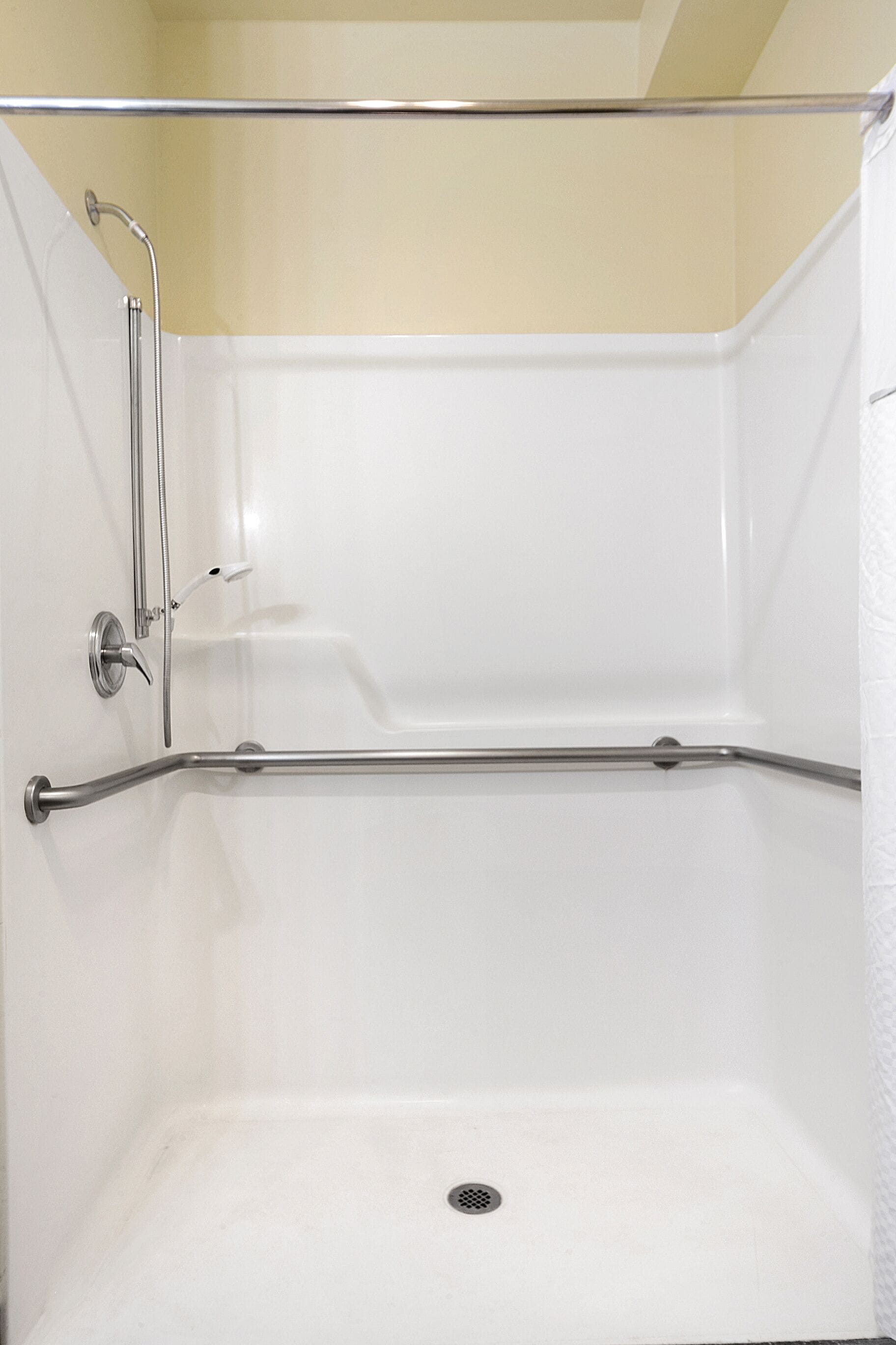 A corner shower with a glass door, a metal grab bar, and a white tiled wall.
