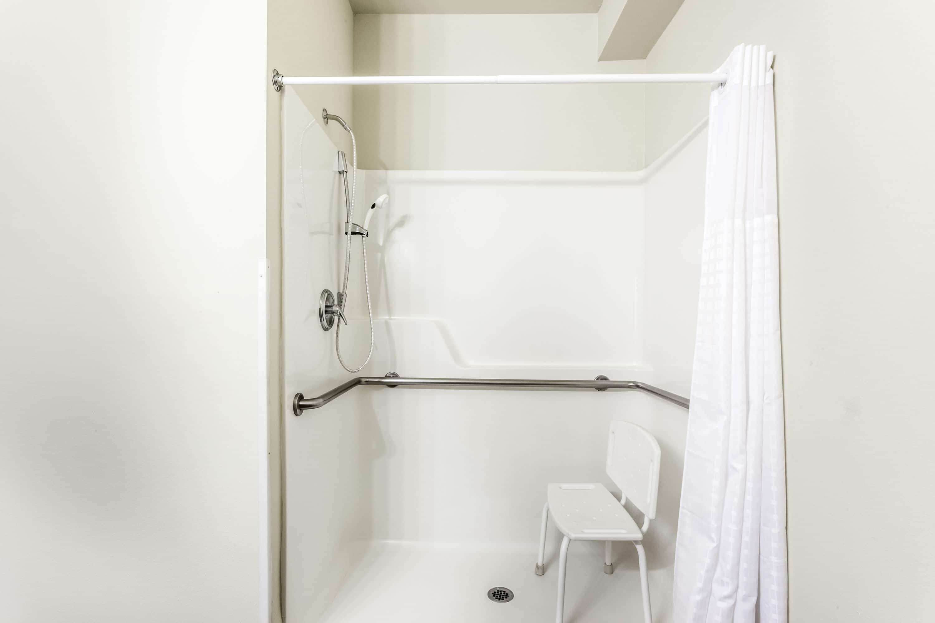 Une douche à l’italienne avec une chaise blanche, une barre d’appui et un pommeau de douche.