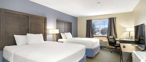 A hotel room with two beds, a desk, a chair, and a TV.