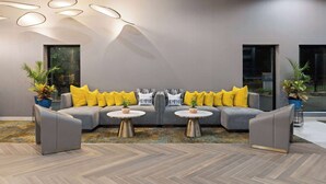 A modern lounge area with a grey sofa and armchairs, two small round tables, and decorative pillows. - La Quinta Inn & Suites by Wyndham Memphis I-240 (Memphis)