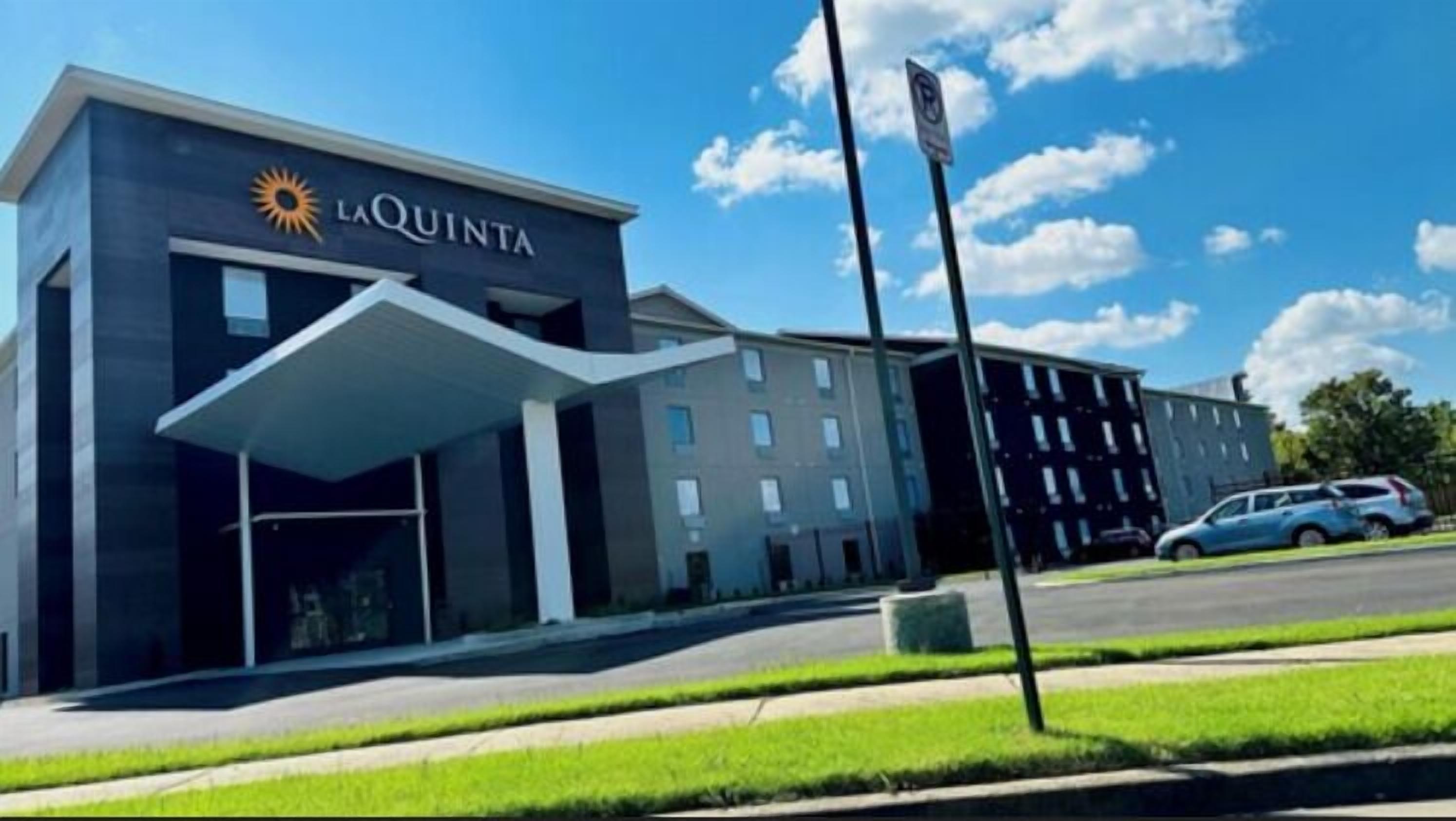 A modern hotel with a covered entrance, a parking area, and a clear blue sky.