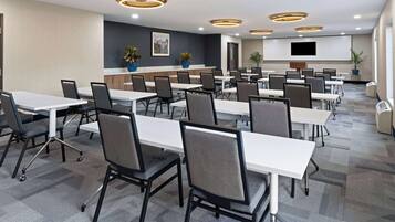 A conference room with multiple tables and chairs, a flat-screen TV mounted on the wall, and ceiling lights.