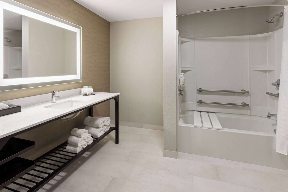 A modern bathroom with a large mirror, two sinks, a shower with glass doors, and a towel rack.