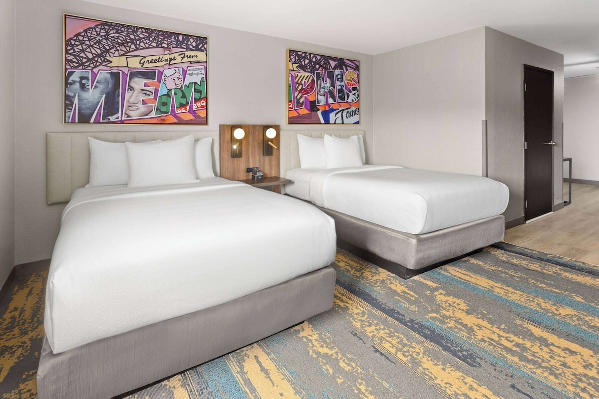 A hotel room with two beds, a nightstand, and two wall-mounted light fixtures.