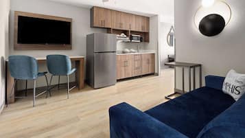 Une cuisine moderne équipée d’un téléviseur à écran plat, de meubles en bois et d’un four à micro-ondes encastré. Le salon comprend un canapé bleu et deux fauteuils assortis.
