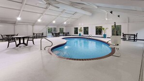An indoor swimming pool with a tiled edge, surrounded by tables and chairs, and large windows. - La Quinta Inn & Suites by Wyndham Memphis I-240 (Memphis)