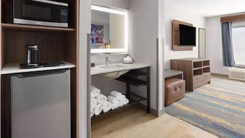 A modern hotel room with a microwave, coffee maker, and neatly folded towels on a shelf.
