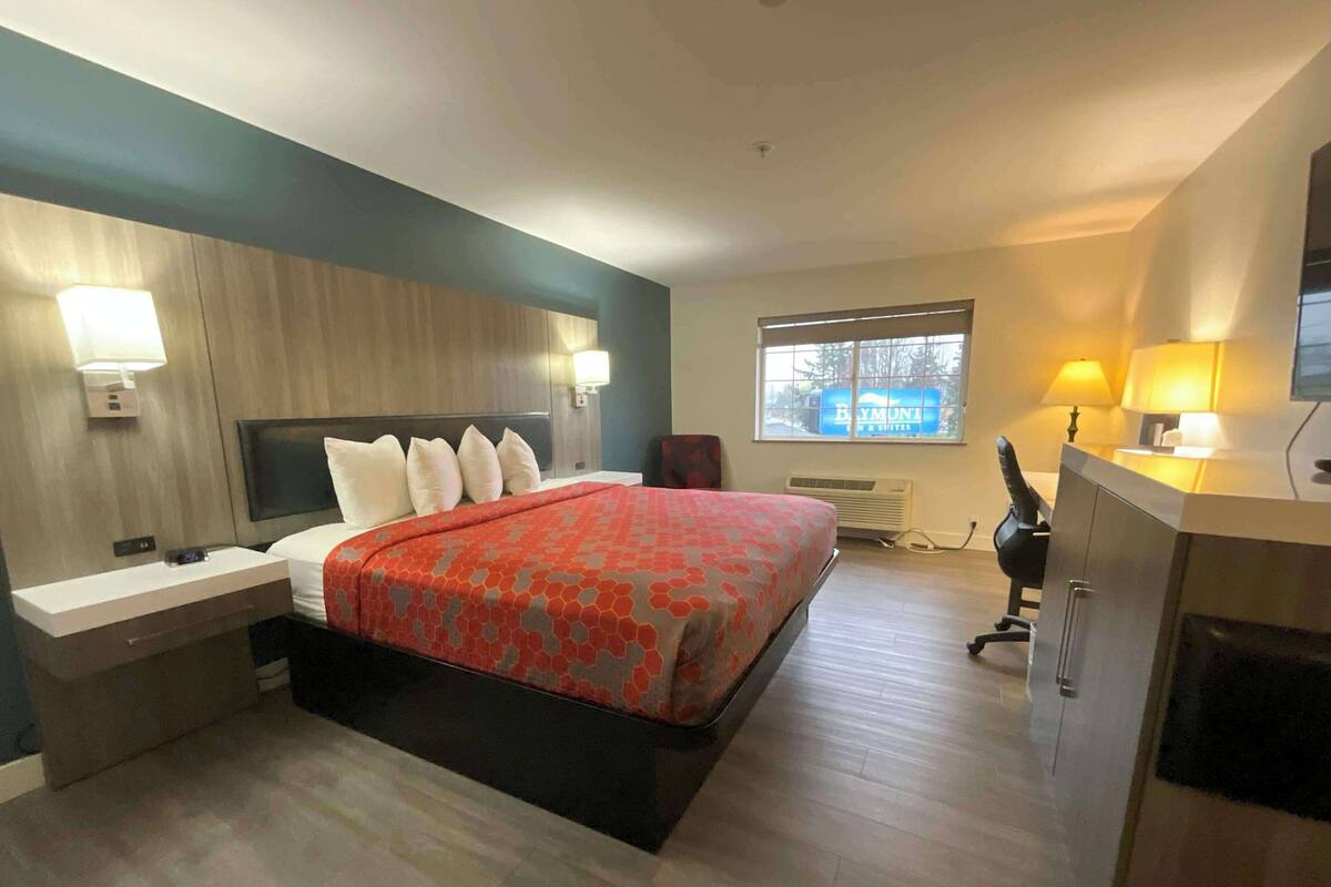 A modern hotel room with a bed, bedside tables, a desk, and a chair.