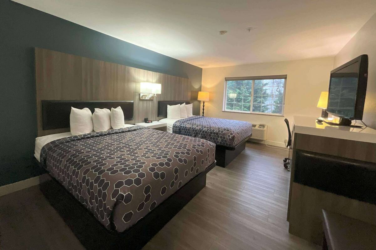 A modern hotel room with two beds, a desk, and a TV.