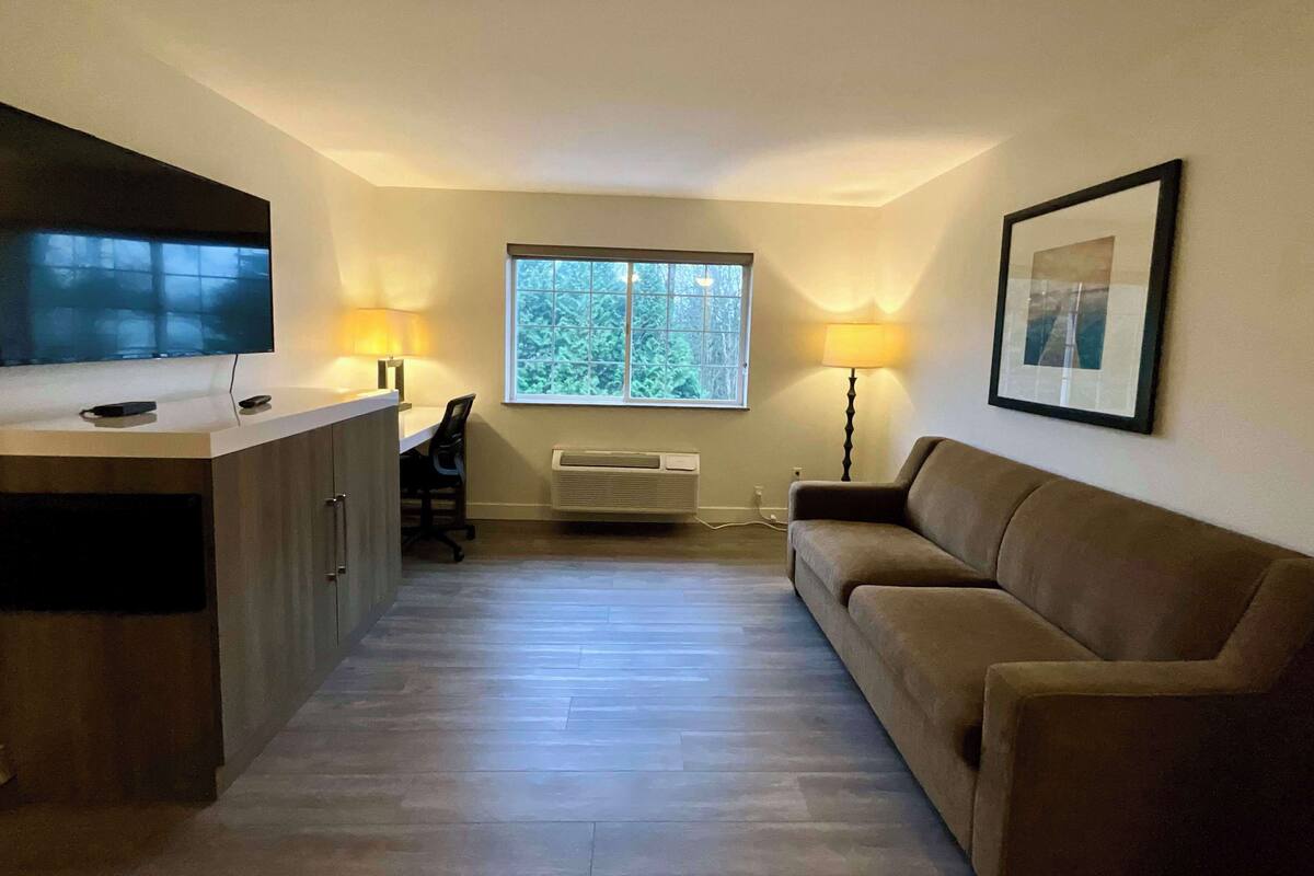 A compact living space with a kitchenette, a large window, a couch, and a flat-screen TV.
