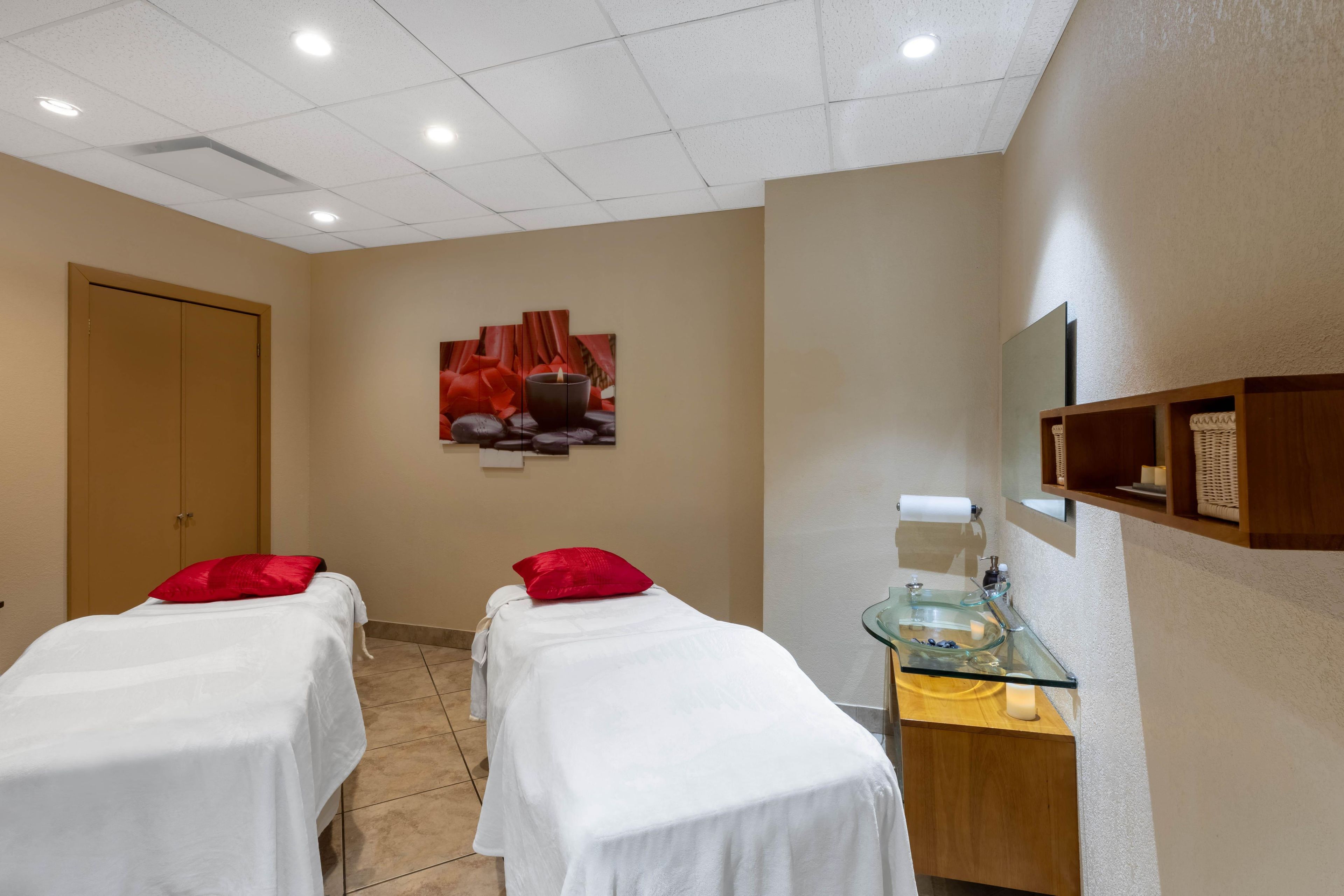 A room with two beds, a massage table, a glass sink, and a wall-mounted shelf.