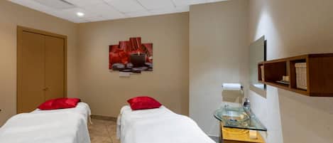 A room with two beds, a massage table, a glass sink, and a wall-mounted shelf.