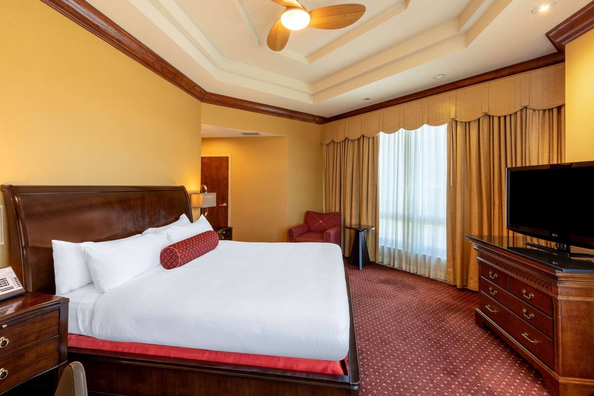 A hotel room with a large bed, a television, a desk with a telephone, and a chair.