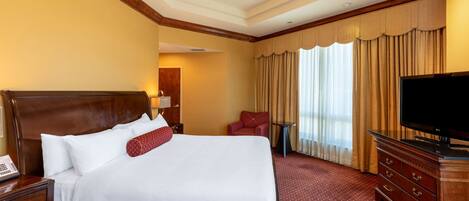 A hotel room with a large bed, a television, a desk with a telephone, and a chair.