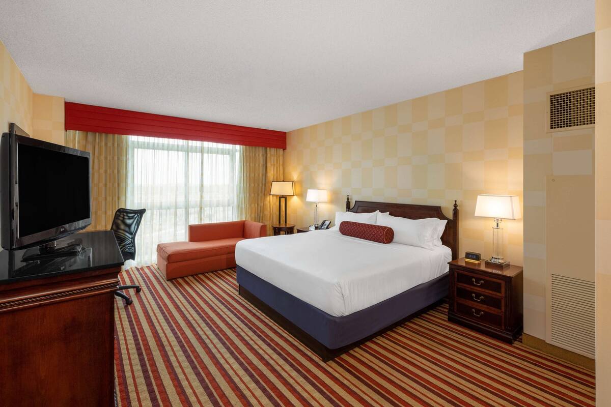A hotel room with a large bed, a TV, a desk, and a chair.