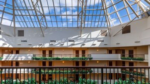 Un atrio de varios niveles con techo de cristal, balcones con plantas y un espacio central abierto.