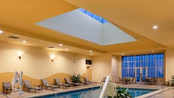 Piscina interna iluminada com luzes no teto, claraboias e espreguiçadeiras.