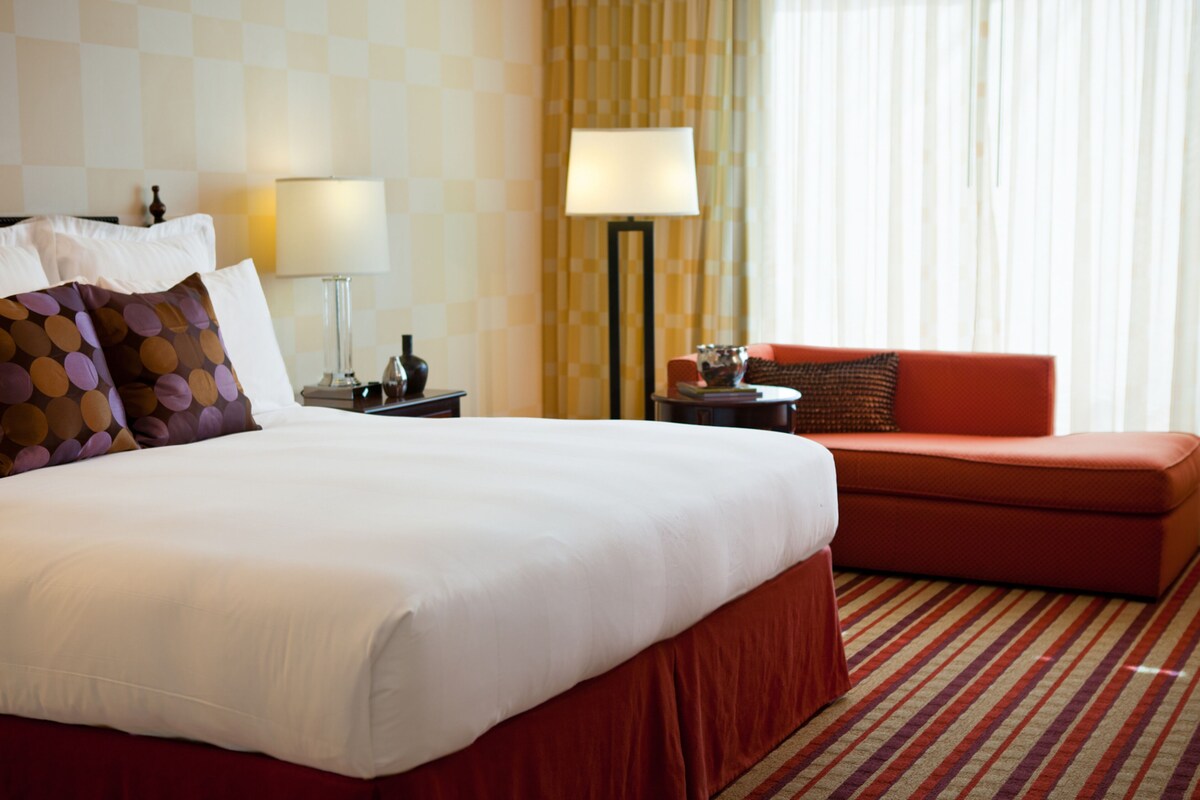 A hotel room with a large bed, a red sofa, a lamp, and a checkered wall.