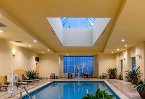 An indoor swimming pool with a skylight, lounge chairs, and potted plants. - Wyndham Grand Oklahoma City Downtown (Oklahoma City)