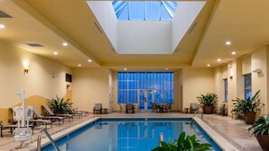 Una piscina interior con tragaluces, sillas de descanso y plantas en macetas.