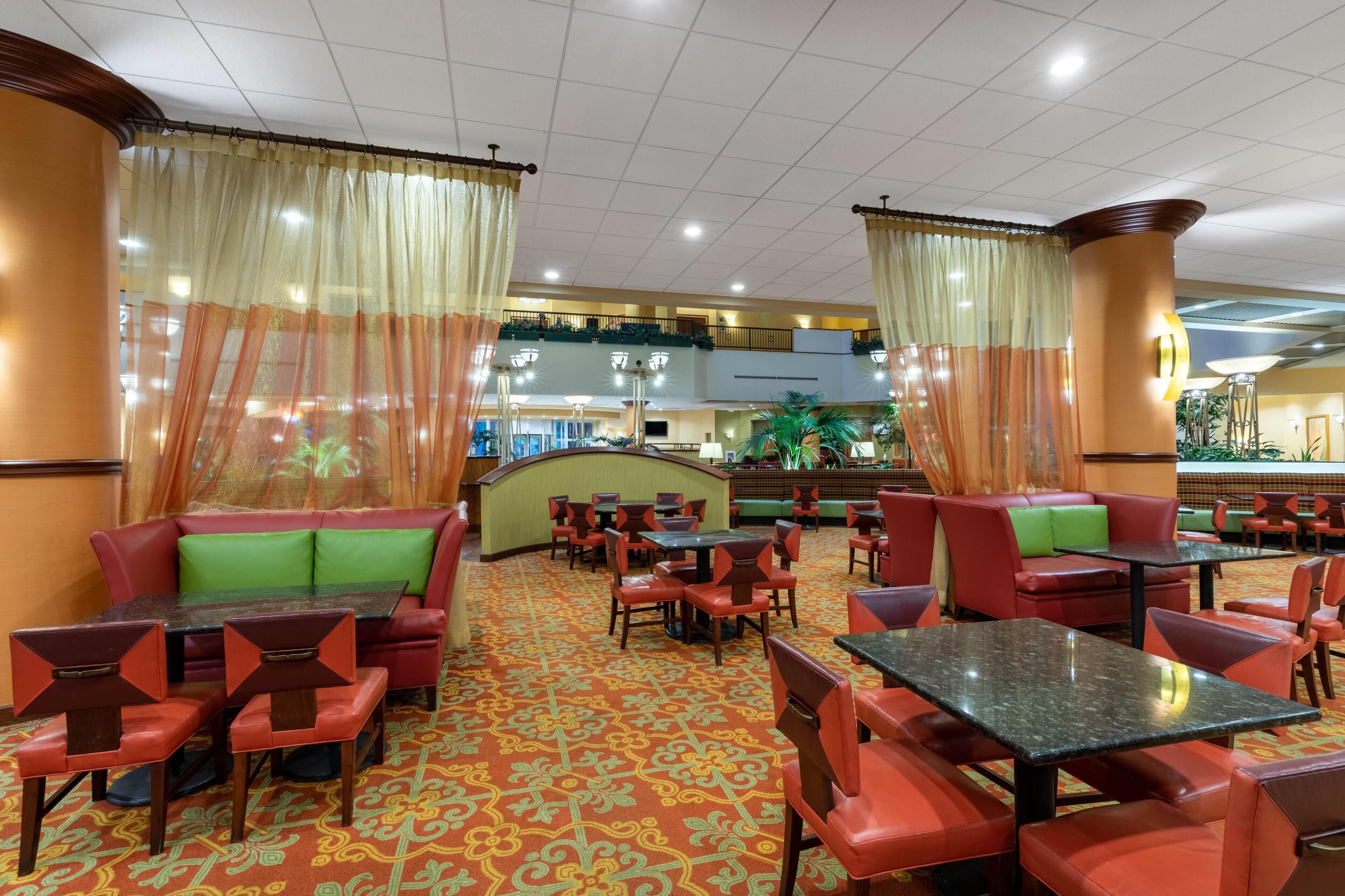 Un hall d’hôtel avec des sièges, des tables et un tapis à motifs, le tout dans des tons de rouge.