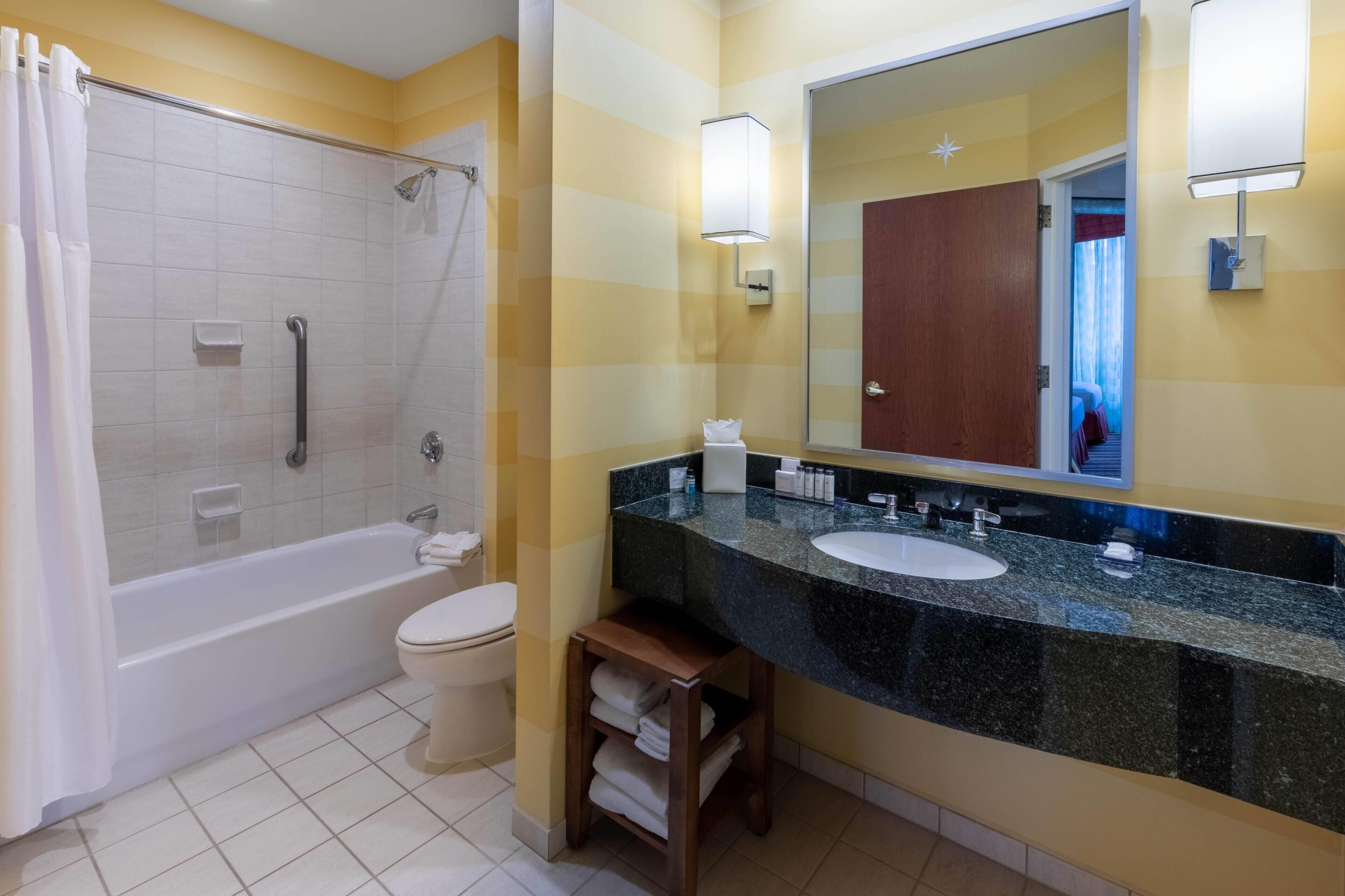 A bathroom with a bathtub, toilet, vanity with a sink, and a large mirror.