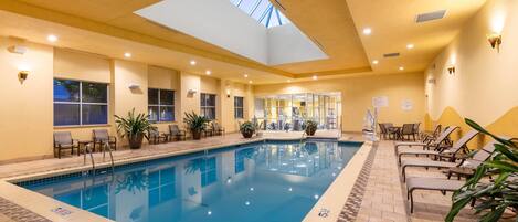 Una piscina interior con tragaluces, sillones de descanso y plantas en macetas.