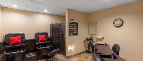 A room with two massage chairs, a reception desk, a clock, and a shelf with various items.