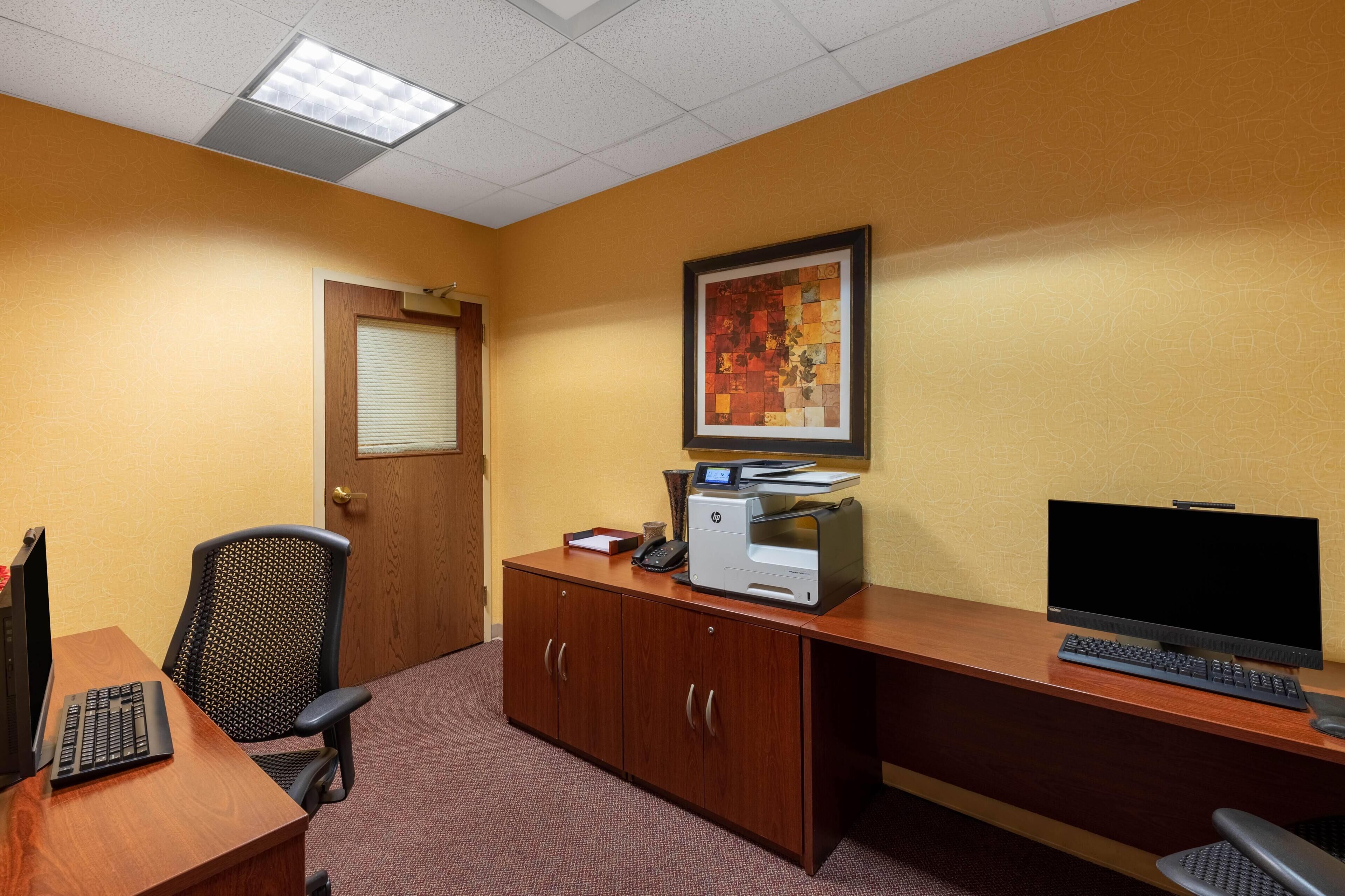 A conference room with a wooden desk, a computer, a printer, and a framed artwork on the wall.